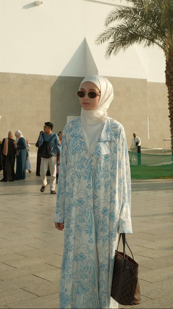 Woman in a light blue dress standing in front of a white building with domes and palm trees.